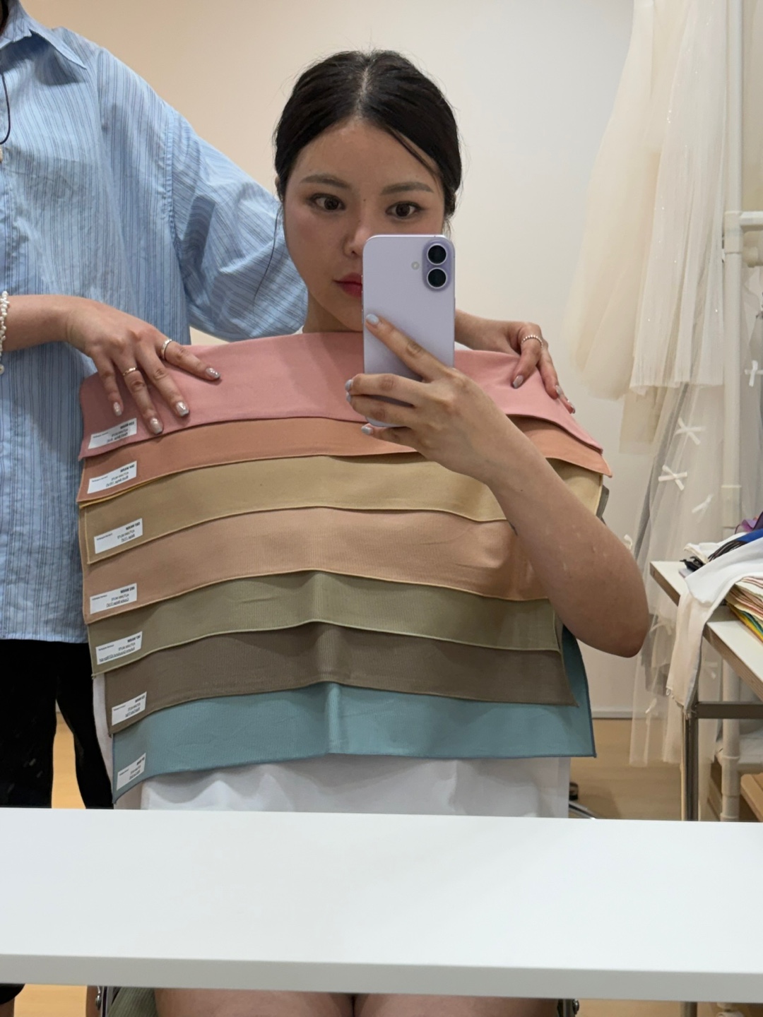 A consultant holding muted-tone drapes against a guest's shoulders in front of the studio mirror